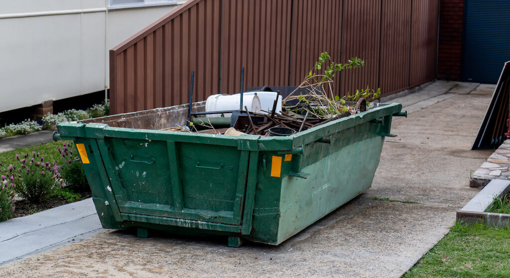 Skip Bin With Household Waste Rubbish On A Front Yard. House Clean Up Concept.